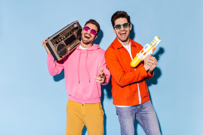 Charming friends in colorful sunglasses have fun on blue background. Excited happy man in yellow pa